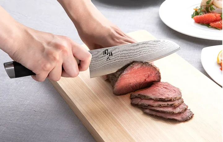 関孫六 ダマスカス 三徳包丁で牛肉を切っている使用シーン。刃に波状のダマスカス模様がはっきり見える