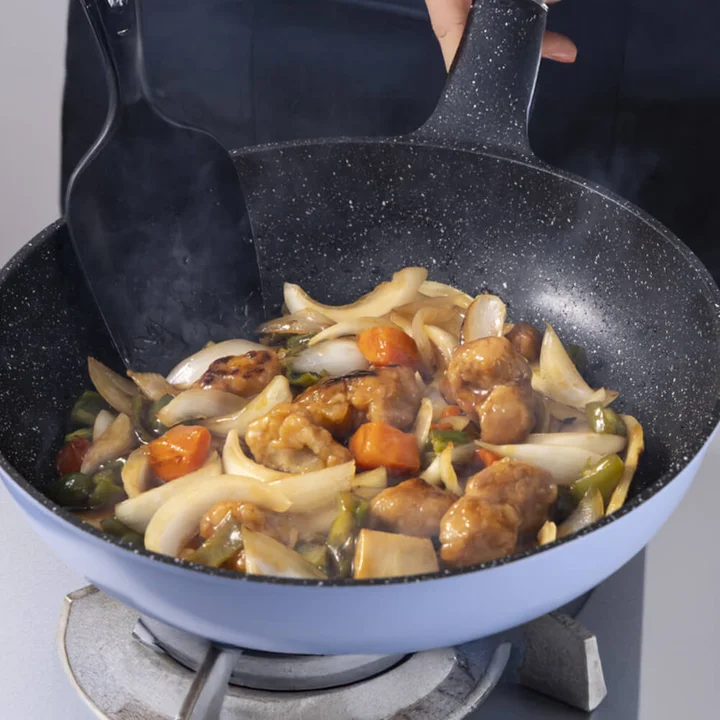 ラクカル フライパンで野菜と肉を炒めているところ。ガスコンロの五徳の上に乗せた状態で、片手で取っ手を持ち上げながらへらで具材を返している