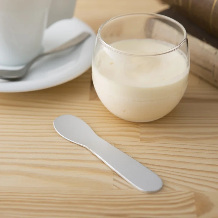 手の熱で溶かしてすくうアイスクリームスプーンと、クリーム色のデザートが入ったグラス