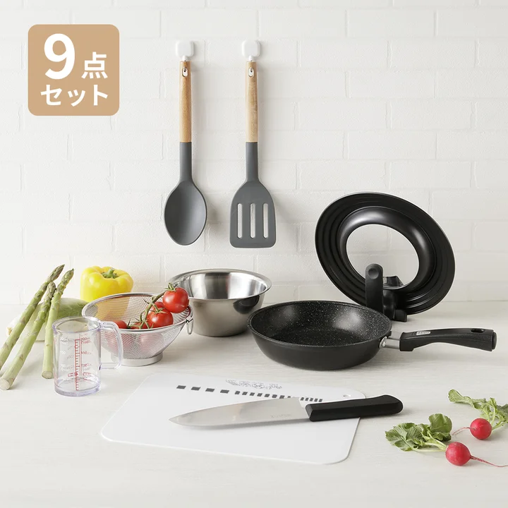 貝印の一人暮らし9点セット。木の柄のシリコーンスプーンとターナー、フライパン20cm、自立するフライパンカバー、ステンレスボール、ざる、計量カップ、三徳包丁、まな板が並んでいる