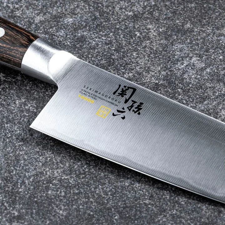 関孫六 10000CC 三徳165mm の刃のアップ。「SEKIMAGOROKU STAINLESS/HIGH-CARBON CLAD STEEL 10000CC」の刻印と、銀色の口金・濃い茶色の積層強化木の柄が見える