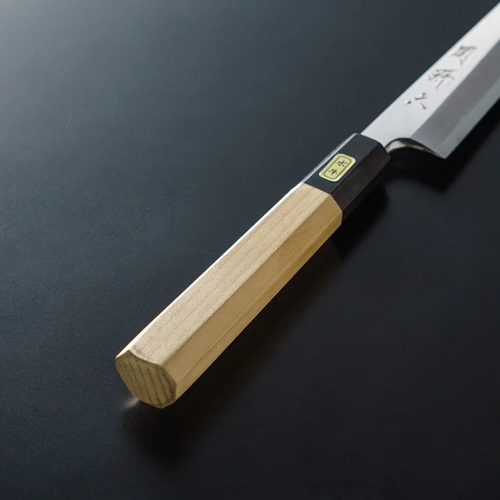 関孫六 青紙鋼(青紙2号) 柳刃 210mm の柄のアップ。白木の八角柄と、黒い水牛角の口金に付いた金色の銘板