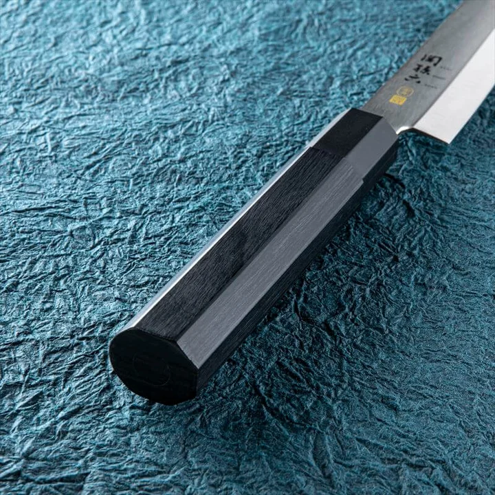 関孫六 金寿ST 和包丁 刺身 210mm の柄のアップ。黒い積層強化木の木目と、刃との境目の口金