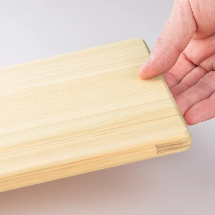 関孫六 軽量桧まな板 の角を手で持ち、厚み約12mmの薄さを確認している様子