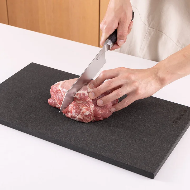 関孫六 マスターラインまな板 L の上で豚肉の塊を包丁で切っている使用シーン