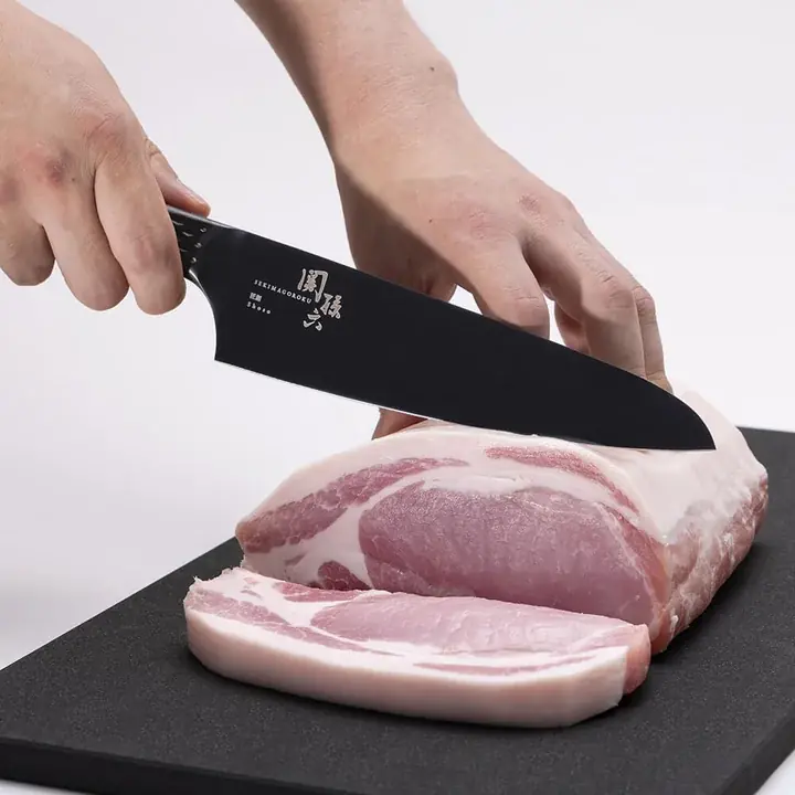 関孫六 匠創 - 漆黒 シェフナイフで豚バラのブロック肉を切っているところ